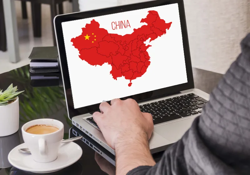 Sobre uma mesa tem um notebook e uma pessoa está com a mão sabre o teclado. Na tela do aparelho tem um mapa da China.