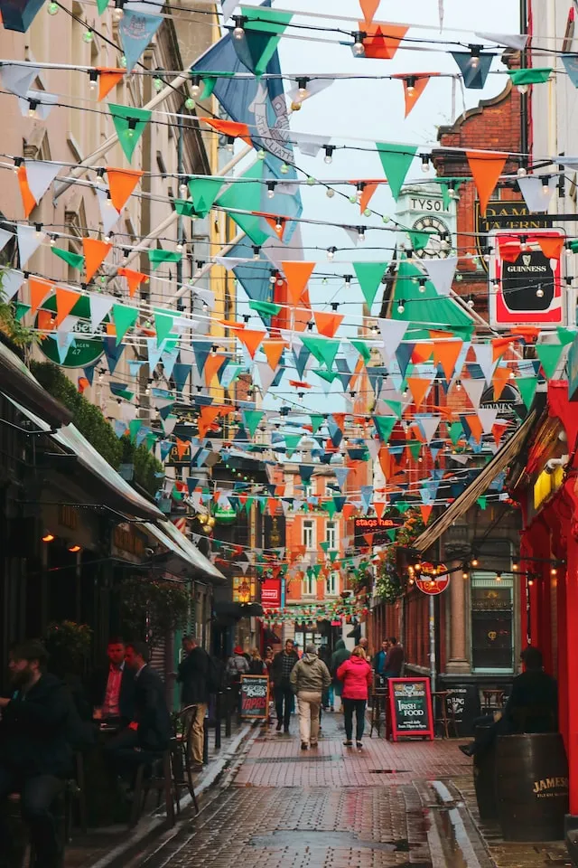 rua cheia de pessoas e com bandeiras com as cores da Irlanda