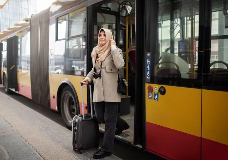 mulher descendo de um ônibus com mala