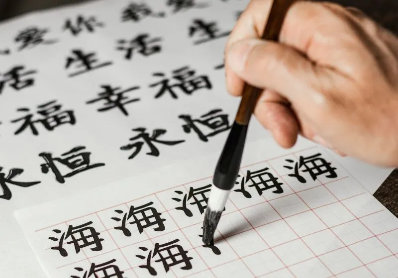 imagem de uma pessoa escrevendo com um pincel em uma folha em Japonês
