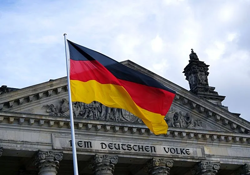 Alemanha Imagem da bandeira da Alemanhã em frente a um prédio histórico ilustrando como conseguir cidadania europeia pelo sobrenome.