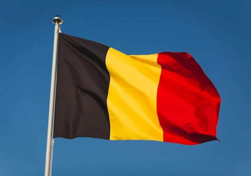 bandeira de Bélgica Imagem da bandeira da Bélgica com céu azul de fundo ilustrando como conseguir cidadania europeia pelo sobrenome.