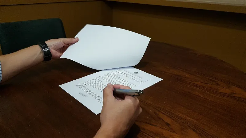 Imagem de pessoa assinando papéis sobre uma mesa escura ilustrando o trabalho do tradutor juramentado.