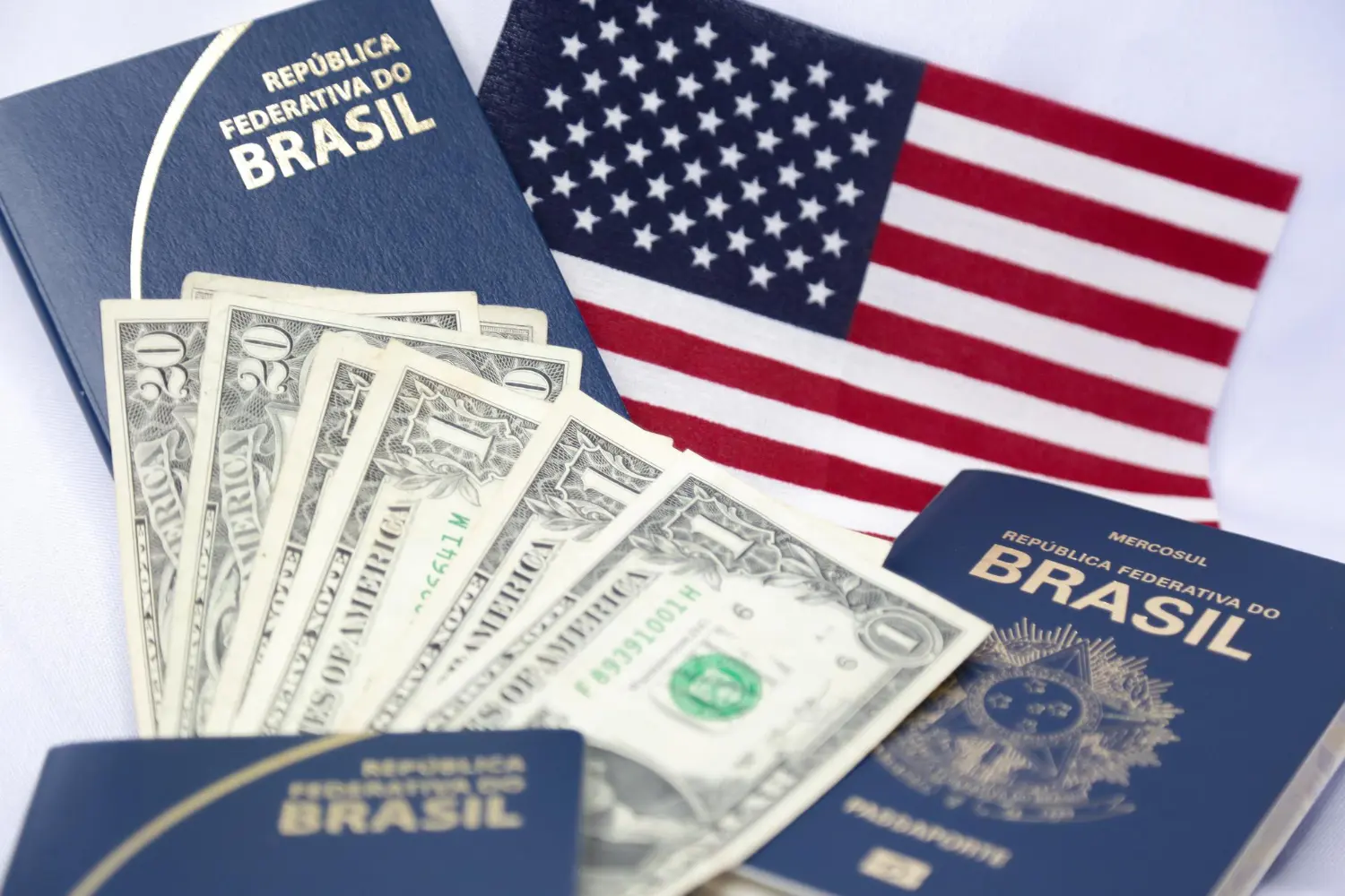 Imagem de três passaportes brasileiros e notas de dólares, junto a uma bandeira dos Estados Unidos, sugerindo a renovação do visto americano para brasileiros.