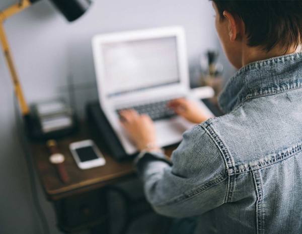 Homem sentado em uma escrivaninha com o notebook aberto enquanto trabalha